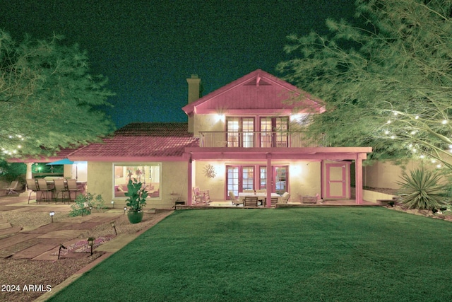 back house at twilight with french doors, an outdoor bar, a patio area, and a yard