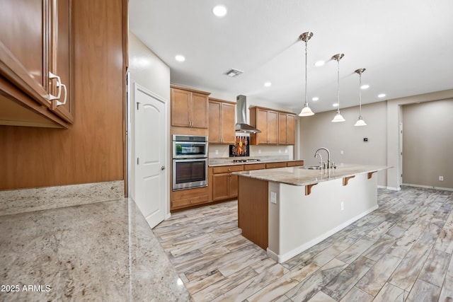 1344 N Claiborne, Mesa, AZ 85205 - kitchen featuring wall chimney exhaust hood, a breakfast bar area, brown cabinets, light stone counters, and stainless steel appliances