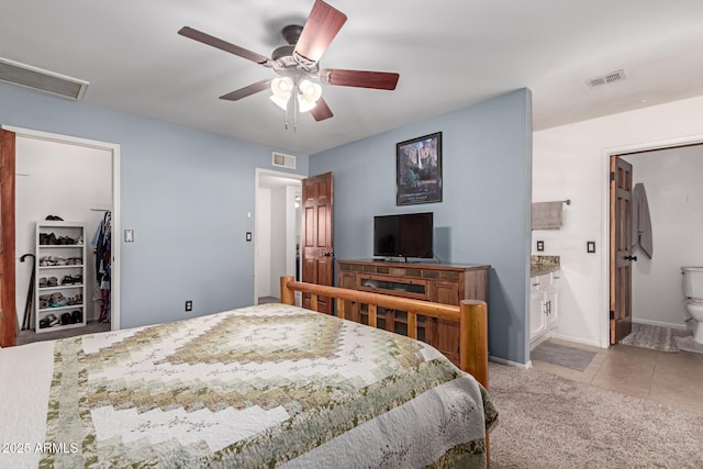 tiled bedroom with ceiling fan, a spacious closet, and ensuite bath