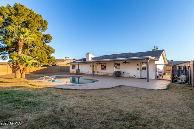 back of property with ceiling fan, a patio, a fenced in pool, and a lawn