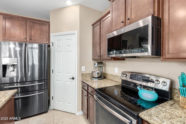 kitchen featuring light stone counters, light tile patterned floors, brown cabinetry, and stainless steel appliances