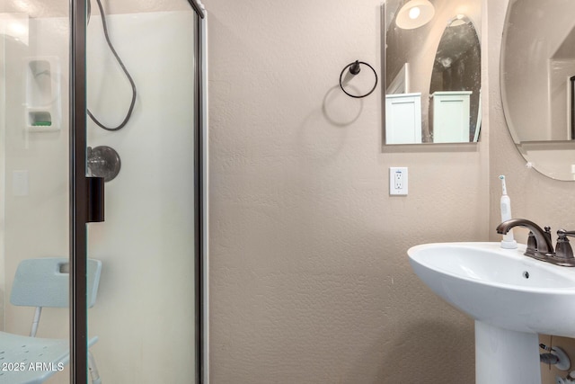 full bathroom featuring a sink, a shower stall, and a textured wall