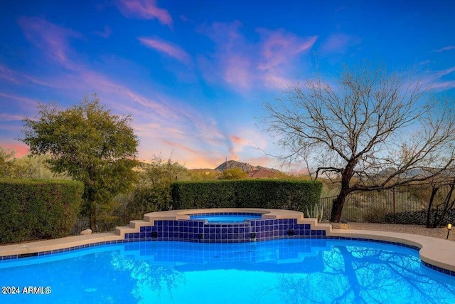 pool at dusk featuring a mountain view and an in ground hot tub