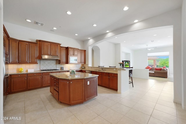 kitchen with stainless steel microwave, black gas stovetop, a kitchen island, a kitchen bar, and kitchen peninsula