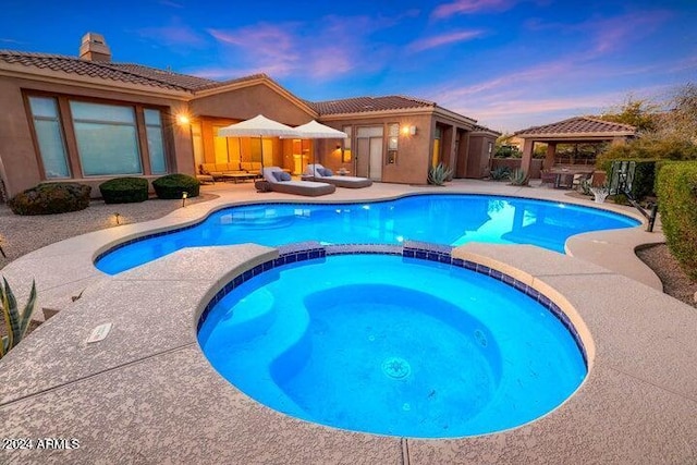 pool at dusk featuring a gazebo, an in ground hot tub, and a patio