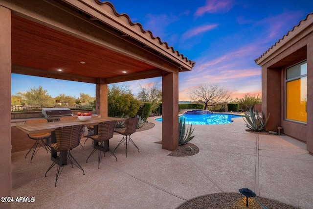 patio terrace at dusk featuring area for grilling and a swimming pool with hot tub