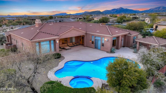 pool at dusk featuring a patio area, an in ground hot tub, and a mountain view