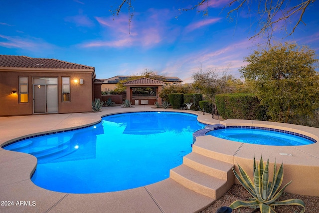 pool at dusk with a gazebo, a patio area, and an in ground hot tub