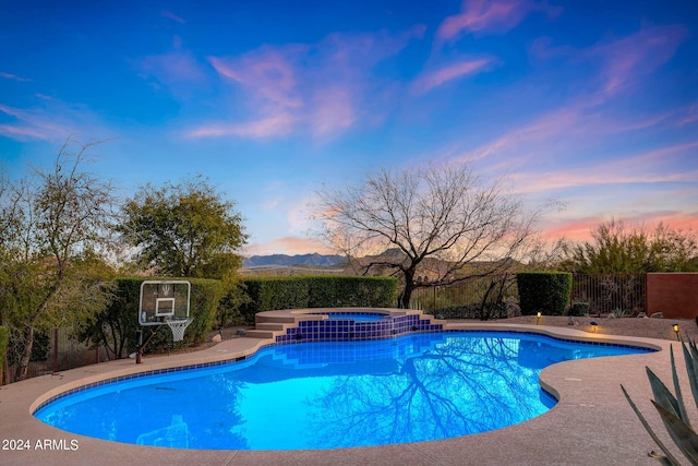 pool at dusk featuring a mountain view and an in ground hot tub