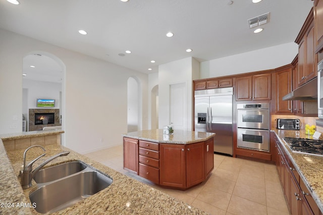 kitchen featuring a center island, sink, light stone countertops, light tile patterned flooring, and stainless steel appliances