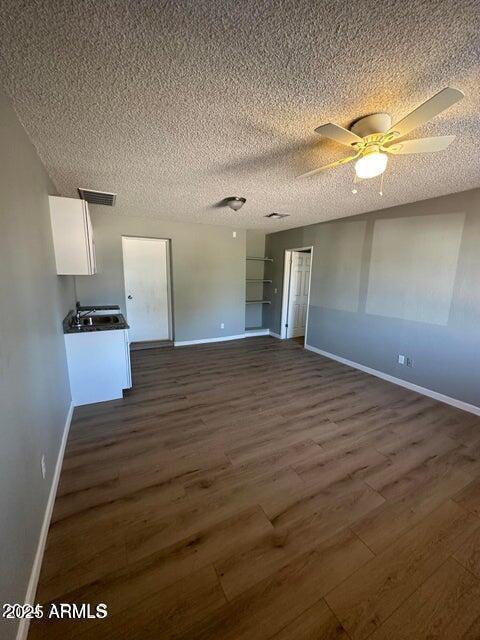 interior space with a textured ceiling, baseboards, visible vents, and dark wood-style floors