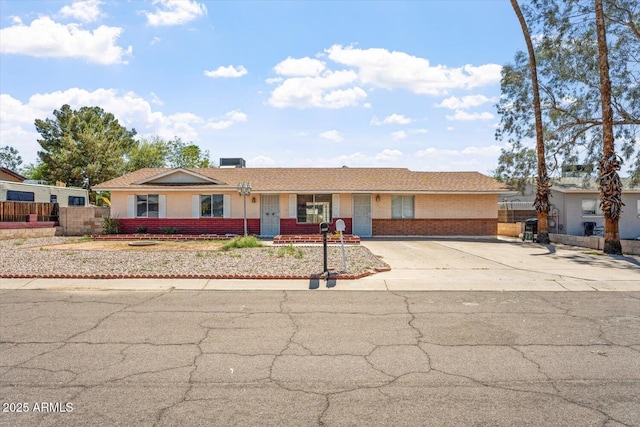 ranch-style house featuring fence, brick siding, and concrete driveway