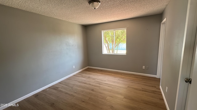 spare room with baseboards, wood finished floors, and a textured ceiling