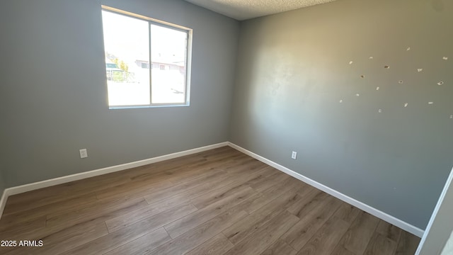 spare room with baseboards, wood finished floors, and a textured ceiling