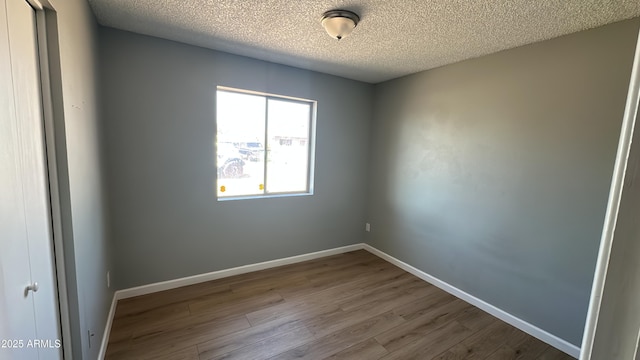 empty room featuring baseboards, wood finished floors, and a textured ceiling