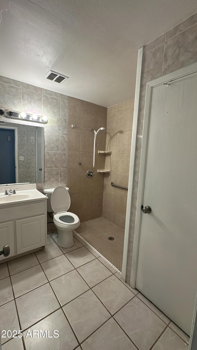 bathroom featuring a textured ceiling, toilet, a tile shower, visible vents, and vanity