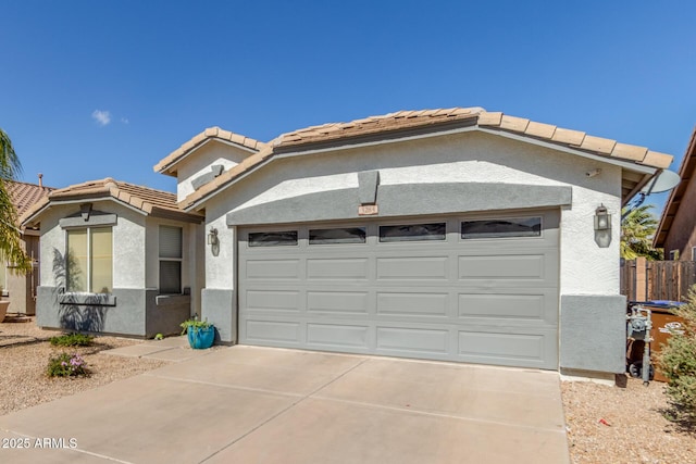 view of front of house featuring an attached garage, a tiled roof, concrete driveway, and stucco siding