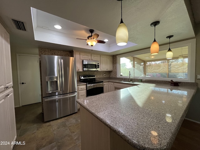 kitchen with appliances with stainless steel finishes, a tray ceiling, sink, stone countertops, and decorative light fixtures