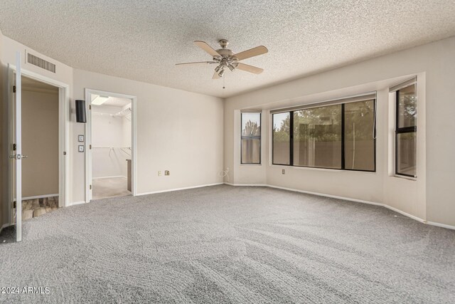 unfurnished bedroom with carpet floors, a walk in closet, ceiling fan, and a textured ceiling