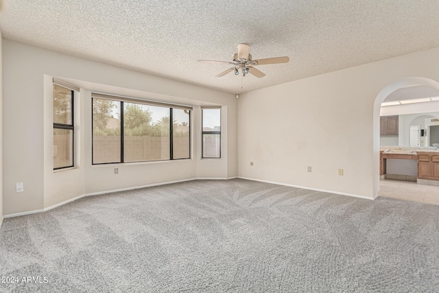 unfurnished room featuring a textured ceiling, ceiling fan, arched walkways, and light carpet