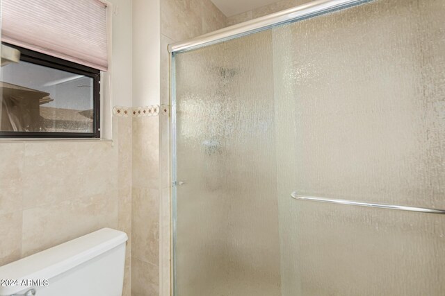 bathroom featuring a shower with door, tile walls, and toilet