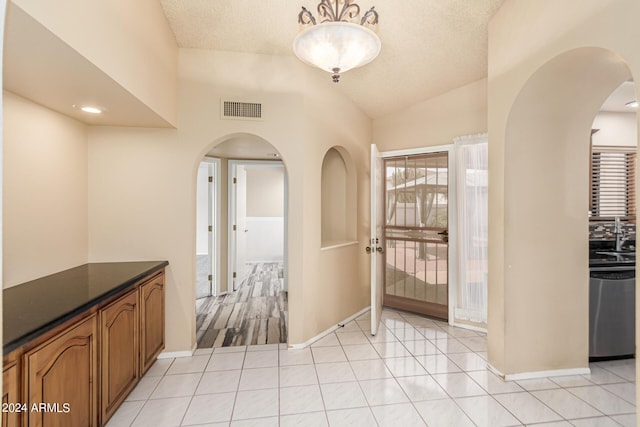 corridor featuring visible vents, vaulted ceiling, arched walkways, light tile patterned flooring, and a textured ceiling