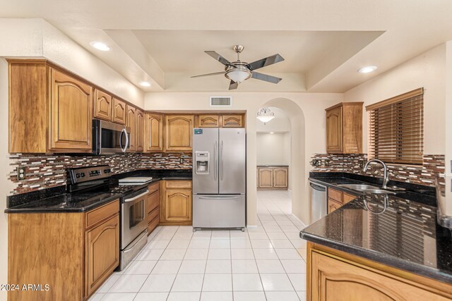 kitchen featuring a tray ceiling, stainless steel appliances, sink, decorative backsplash, and ceiling fan