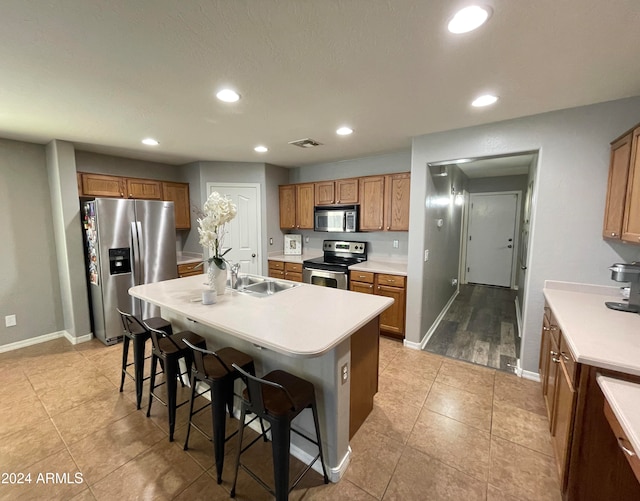 kitchen with a breakfast bar, appliances with stainless steel finishes, a center island with sink, and sink