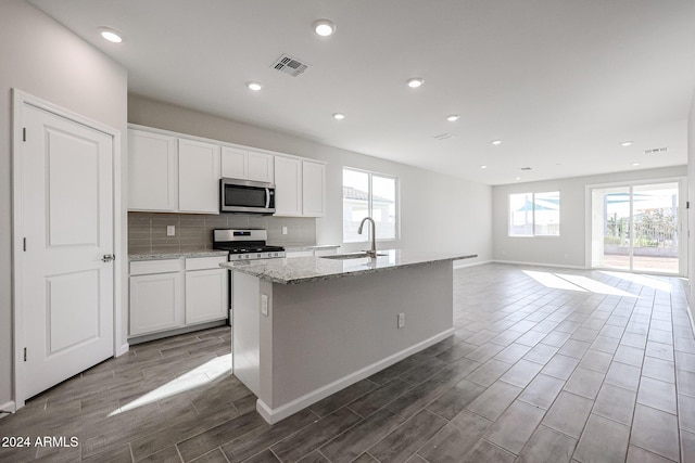 kitchen with white cabinetry, sink, backsplash, a center island with sink, and appliances with stainless steel finishes