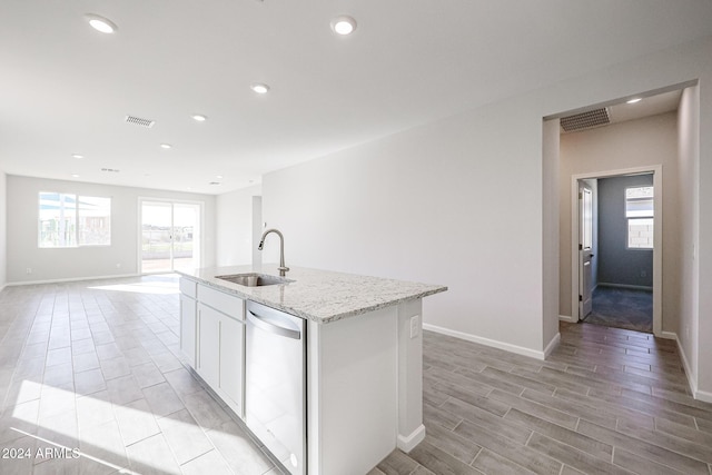 kitchen featuring dishwasher, a kitchen island with sink, sink, light stone counters, and white cabinetry