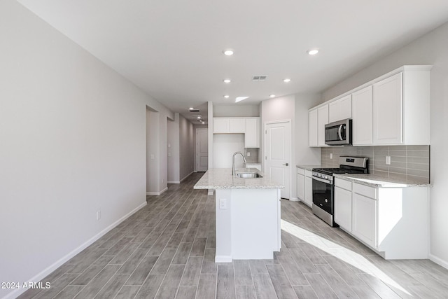 kitchen with sink, light stone counters, an island with sink, white cabinets, and appliances with stainless steel finishes