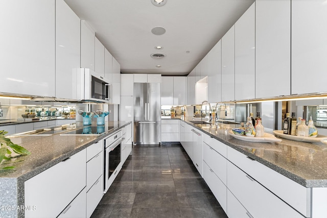 kitchen with appliances with stainless steel finishes, modern cabinets, a sink, white cabinets, and dark stone counters