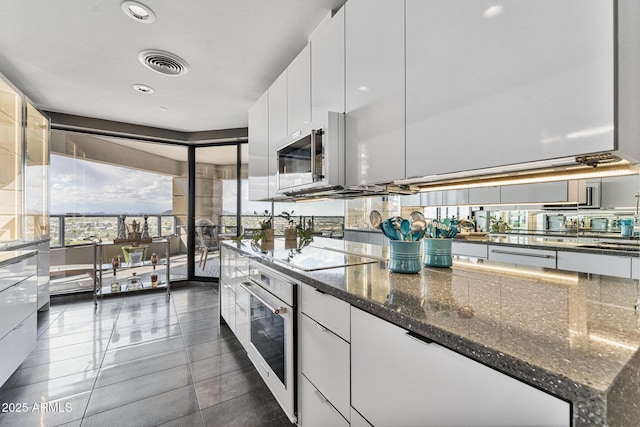 kitchen featuring visible vents, oven, black electric stovetop, white cabinetry, and dark stone countertops
