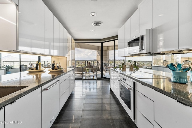 kitchen featuring oven, stainless steel microwave, white cabinetry, and a wealth of natural light