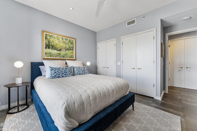 bedroom featuring two closets, baseboards, visible vents, and wood finished floors