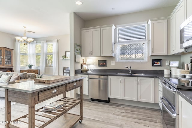 kitchen featuring a notable chandelier, dark countertops, appliances with stainless steel finishes, white cabinetry, and a sink