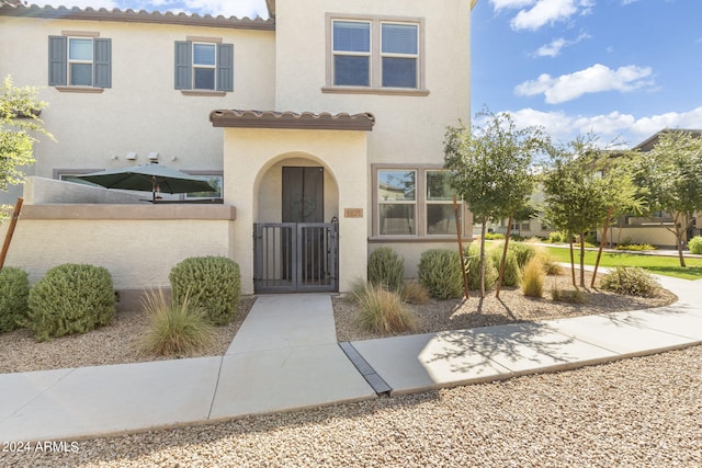 view of exterior entry with a gate, fence, a tiled roof, and stucco siding