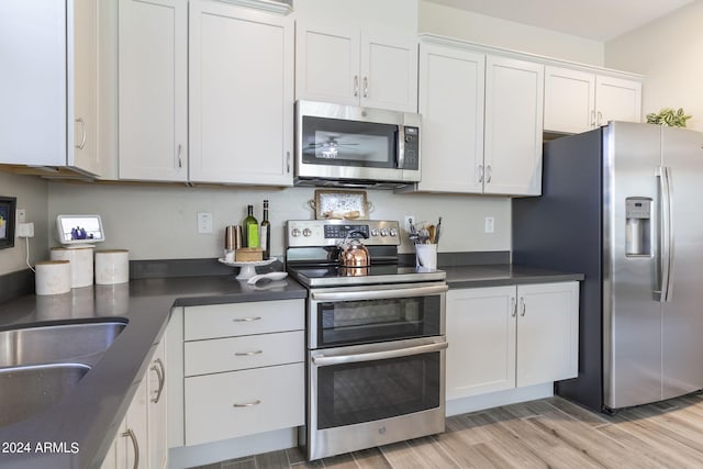 kitchen with dark countertops, light wood-type flooring, appliances with stainless steel finishes, and white cabinets