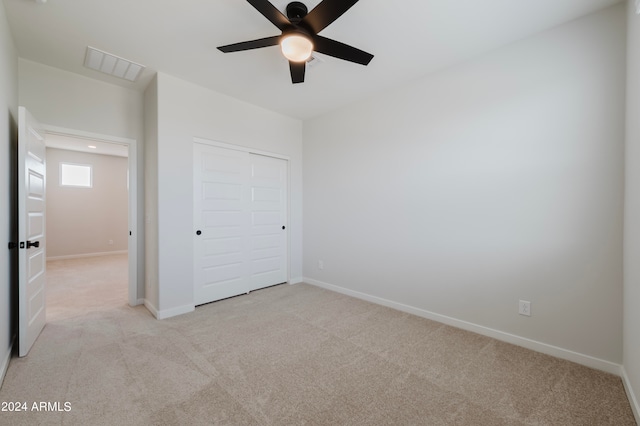 unfurnished bedroom with ceiling fan, light carpet, and a closet