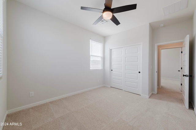 unfurnished bedroom with ceiling fan, light carpet, and a closet