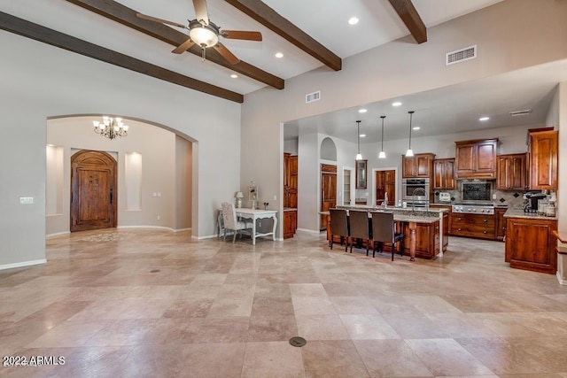 kitchen with a kitchen bar, stainless steel appliances, pendant lighting, beam ceiling, and an island with sink