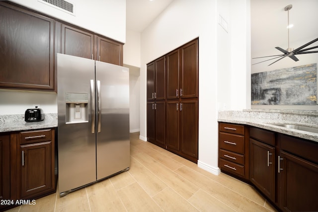 kitchen featuring light stone counters, dark brown cabinets, stainless steel fridge, ceiling fan, and light hardwood / wood-style floors