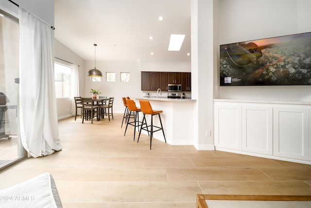 kitchen with light hardwood / wood-style flooring, hanging light fixtures, a kitchen breakfast bar, dark brown cabinetry, and light stone countertops