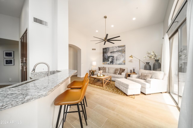 living room with a towering ceiling, ceiling fan, and light wood-type flooring