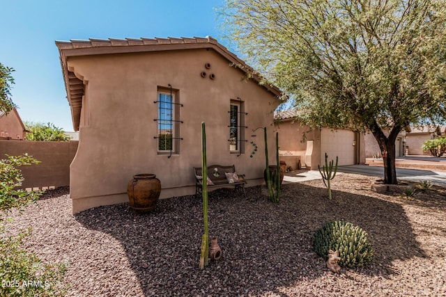 view of side of property featuring concrete driveway, fence, an attached garage, and stucco siding