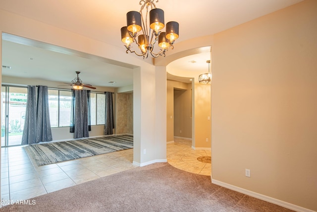 carpeted empty room featuring baseboards, ceiling fan with notable chandelier, arched walkways, and tile patterned flooring