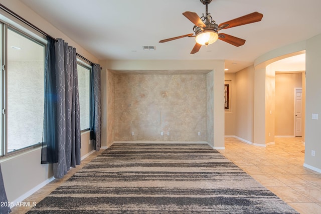 spare room featuring visible vents, baseboards, ceiling fan, arched walkways, and plenty of natural light