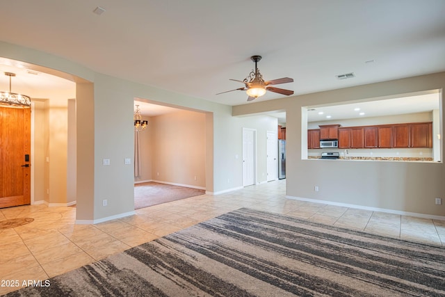 unfurnished living room featuring light tile patterned floors, visible vents, baseboards, arched walkways, and ceiling fan with notable chandelier