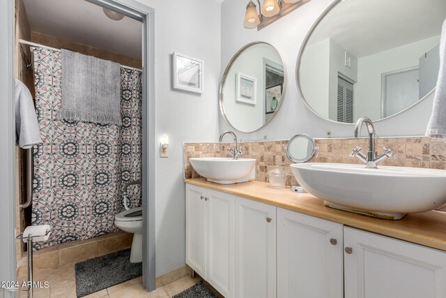 bathroom featuring tile patterned flooring, toilet, decorative backsplash, and vanity