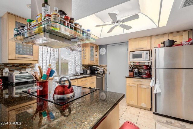 kitchen with ceiling fan, dark stone counters, tasteful backsplash, appliances with stainless steel finishes, and sink